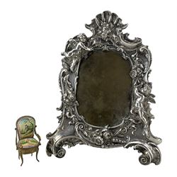19th/ early 20th century silver-plated picture frame, cast with Putti, flower garlands and shell motifs on two scroll feet, with easel strut support, H26cm x W20cm, together with a Continental miniature gilt metal and enamel armchair, H7.5cm (2)