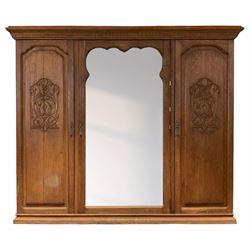 Late 19th century oak triple wardrobe, wide central bevelled mirror door, flanked by two panelled doors each carved with scrolling leaves and flower heads, on moulded skirt base 