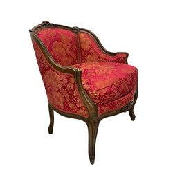 Late 20th century French design stained beech framed armchair and matching stool - the armchair with shaped and moulded frame carved with flower heads and foliage, upholstered in silk red and gold ground fabric with floral pattern, on scroll carved cabriole feet decorated with flower head carvings (W73cm, H82cm, D75cm); the footstool of concaved rectangular form with moulded frame carved with flower heads, upholstered loose cushion, on cabriole feet (70cm x 64cm, H48cm)