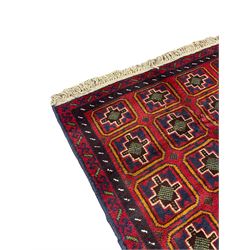 Baluchi crimson ground rug, the field decorated with four columns of square panels each containing stylised rood motifs, the double banded border with indigo shapes
