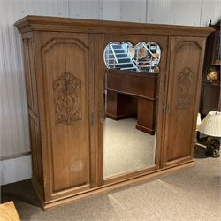 Late 19th century oak triple wardrobe, wide central bevelled mirror door, flanked by two panelled doors each carved with scrolling leaves and flower heads, on moulded skirt base 