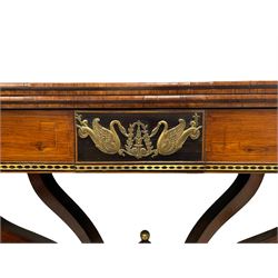 Regency inlaid rosewood card table, rectangular swivel and fold-over top with rounded corners and baize lined interior, the frieze decorated with a central ebony panel with applied gilt metal swan motifs, over a brass inlay band, raised on S-scroll supports united by concave platform base, terminating to out-splayed supports with brass cups and castors