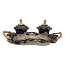 19th century porcelain inkstand, the oblong twin handled base centrally painted with a floral bouquet, flanked by two footed inkwells and covers, with rococo-inspired acanthus moulded borders and handles, pattern no. 2/3339, L26.5cm 