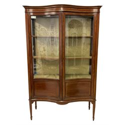 Edwardian inlaid mahogany serpentine display cabinet, projecting cornice over satinwood banding and stringing, enclosed by two glazed serpentine doors with panels to base, raised on square tapering supports with spade feet