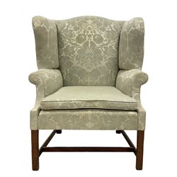 Georgian mahogany framed wingback armchair, upholstered in floral pattern silk damask fabric, wide seat enclosed by rolled arms, on chamfered square supports united by plain stretchers 