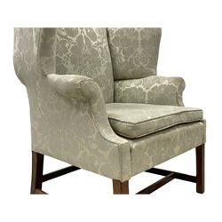 Georgian mahogany framed wingback armchair, upholstered in floral pattern silk damask fabric, wide seat enclosed by rolled arms, on chamfered square supports united by plain stretchers 