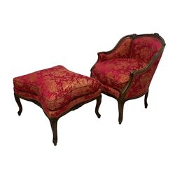 Late 20th century French design stained beech framed armchair and matching stool - the armchair with shaped and moulded frame carved with flower heads and foliage, upholstered in silk red and gold ground fabric with floral pattern, on scroll carved cabriole feet decorated with flower head carvings (W73cm, H82cm, D75cm); the footstool of concaved rectangular form with moulded frame carved with flower heads, upholstered loose cushion, on cabriole feet (70cm x 64cm, H48cm)