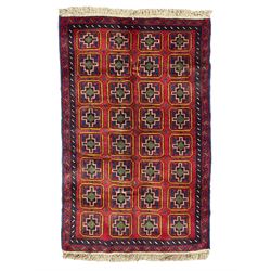 Baluchi crimson ground rug, the field decorated with four columns of square panels each containing stylised rood motifs, the double banded border with indigo shapes