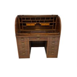 20th century mahogany desk, the roll top opening to reveal interior with drawers, pigeon holes and pull our writing surface over nine drawers, raised on recessed castors W123cm, H127cm, D71cm 