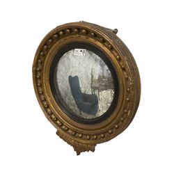 Regency giltwood and gesso framed circular convex wall mirror, the stepped cavetto frame decorated with leafage and applied spheres, with inner ebonised reeded slip, over a foliate and scalloped terminal