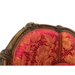 Late 20th century French design stained beech framed armchair and matching stool - the armchair with shaped and moulded frame carved with flower heads and foliage, upholstered in silk red and gold ground fabric with floral pattern, on scroll carved cabriole feet decorated with flower head carvings (W73cm, H82cm, D75cm); the footstool of concaved rectangular form with moulded frame carved with flower heads, upholstered loose cushion, on cabriole feet (70cm x 64cm, H48cm)