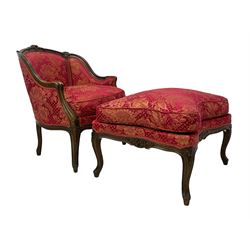 Late 20th century French design stained beech framed armchair and matching stool - the armchair with shaped and moulded frame carved with flower heads and foliage, upholstered in silk red and gold ground fabric with floral pattern, on scroll carved cabriole feet decorated with flower head carvings (W73cm, H82cm, D75cm); the footstool of concaved rectangular form with moulded frame carved with flower heads, upholstered loose cushion, on cabriole feet (70cm x 64cm, H48cm)