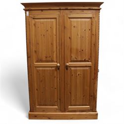 Pine double wardrobe, projecting cornice over two panelled doors, fitted with hanging rail, on plinth base